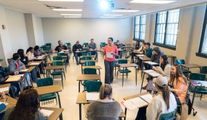Students surrounding professor in a classroom setting while professor is teaching.