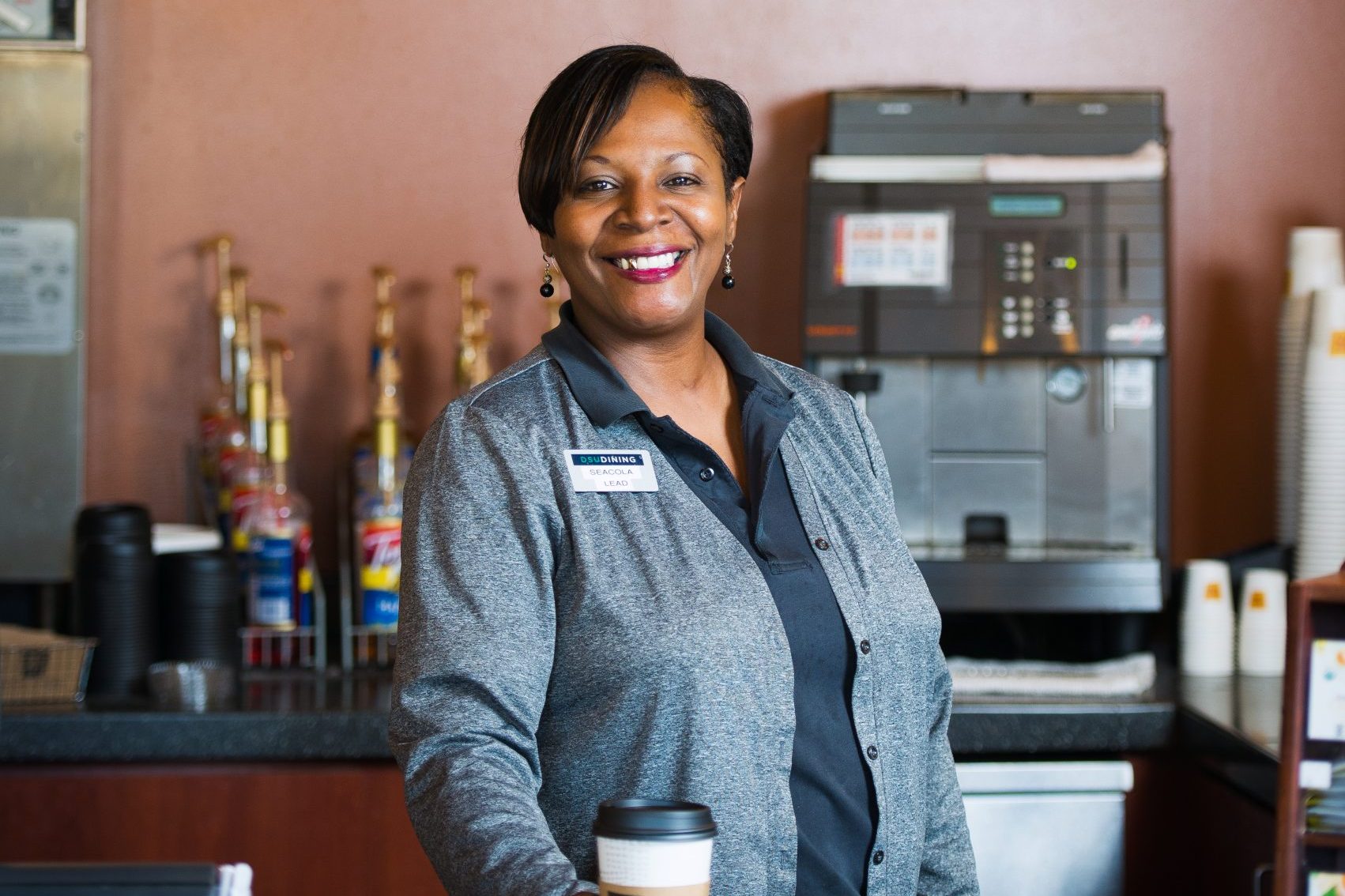 Woman behind coffee shop counter holding a coffee cup.