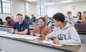Students sitting together in a classroom, smiling and discussing notes during class.
