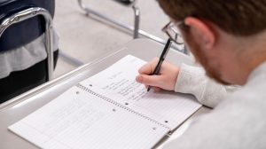 Student sitting at desk writing notes in tablet.