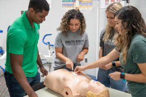 A group of four people gathered around a medical training mannequin placing electrodes on the mannequin.