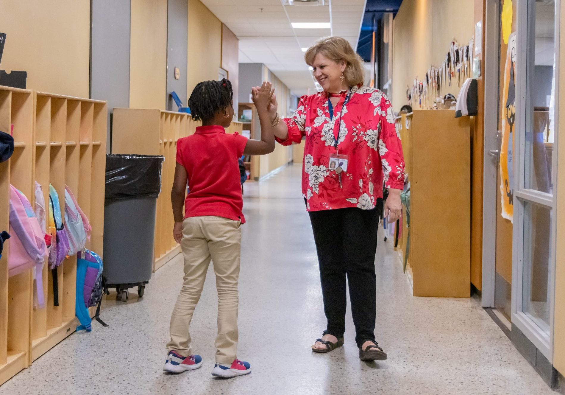 School administrator giving an elementary student a high-five in the hallway.