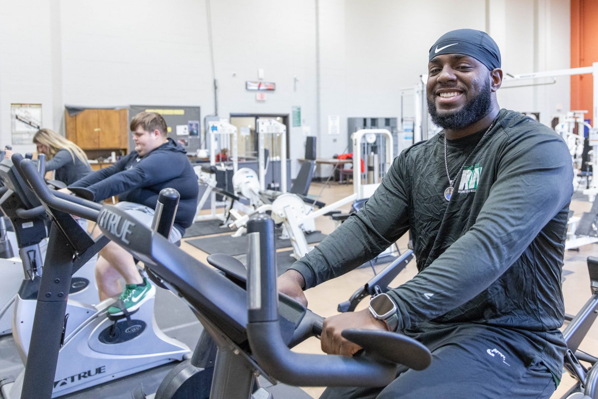 A man on a cycling machine in a fitness center with two other people also on cycling machines behind him.