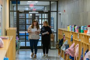 Two administrators walking down a school hallway while reviewing notes their holding in their hands.
