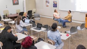 Students and instructor observing two classmates participate in a role-play activity during class.