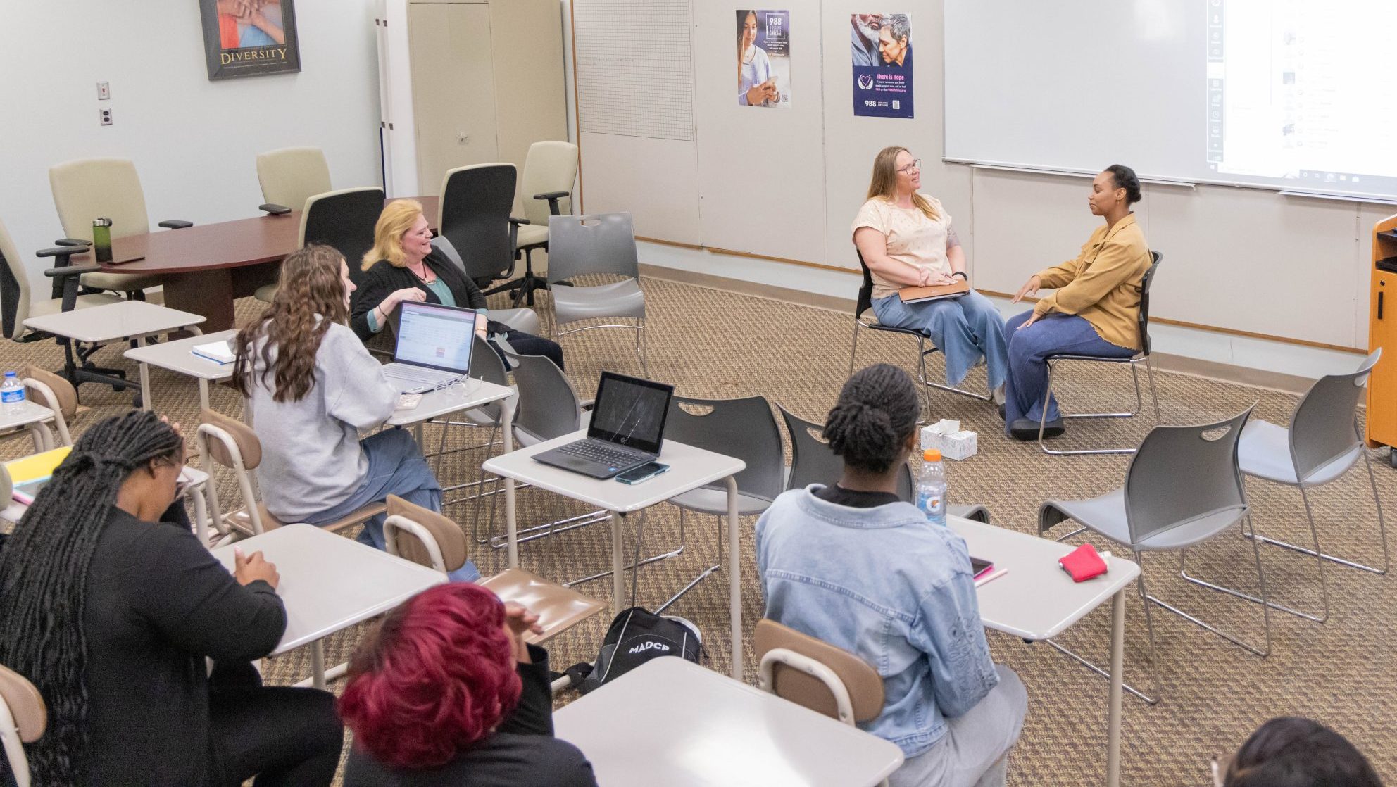 Students and instructor observing two classmates participate in a role-play activity during class.
