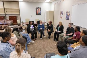 A large group of students with an instructor sitting in a circle engaged in a class activity.