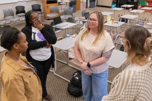 Small group of students standing and talking in a classroom.