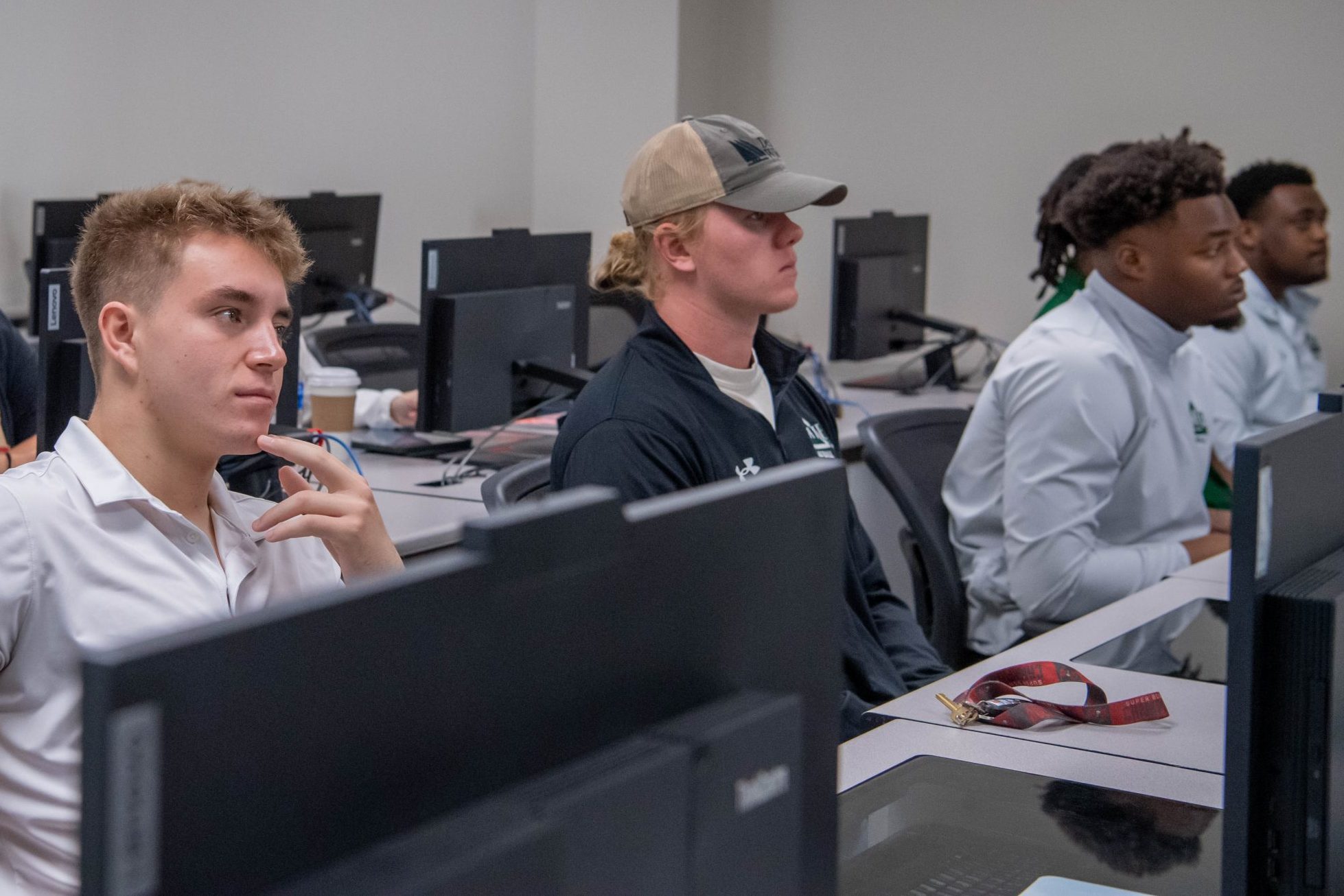 Students sitting at computer desks in a classroom, attentively listening during a lesson.