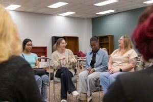 Students seated in a circle engaged in a group discussion in a classroom.