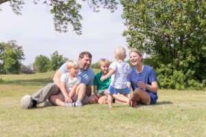 Family with young children sitting together outdoors and interacting.