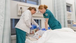 Nursing students practicing bedside patient care in a healthcare simulation lab.