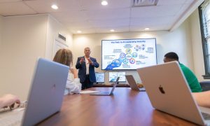 Instructor leads a classroom discussion on artificial intelligence leadership and governance as students follow along on laptops.