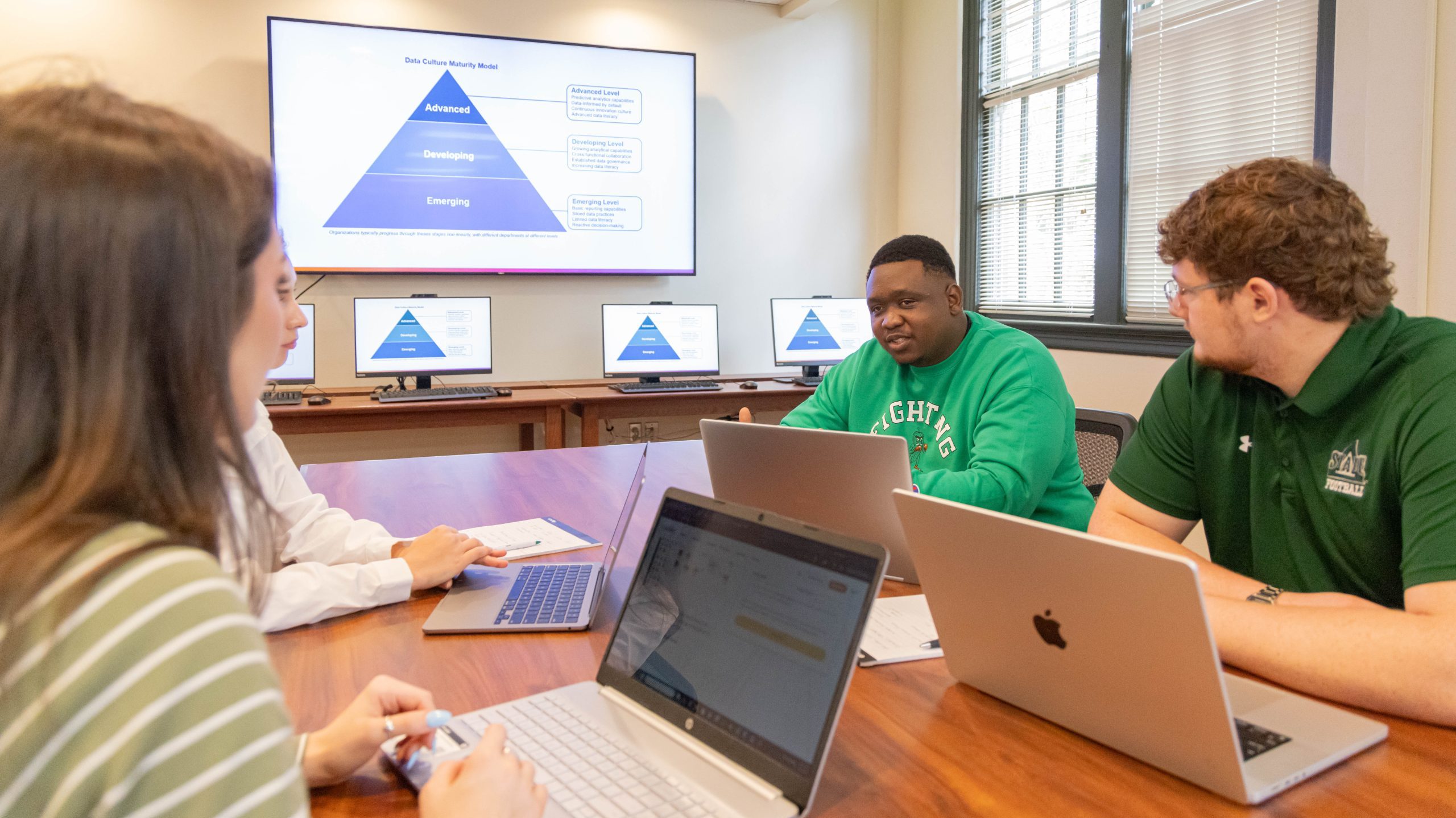 Student collaborate during an artificial intelligence and data leadership class while reviewing a presentation on organizational data maturity.