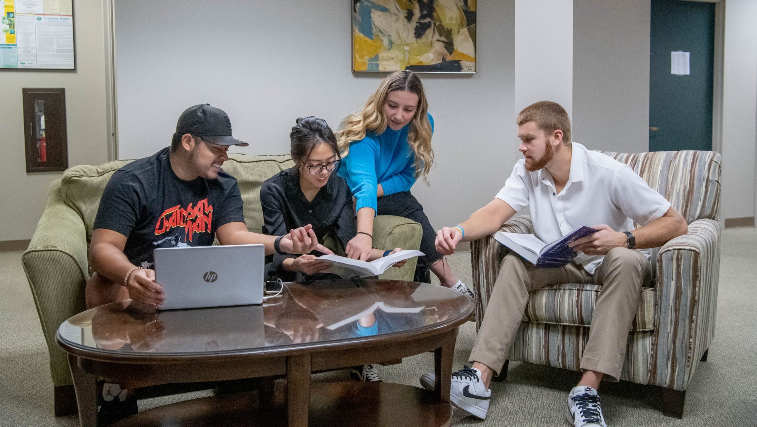 Students gathered around a table in a sitting area with a book and laptop.