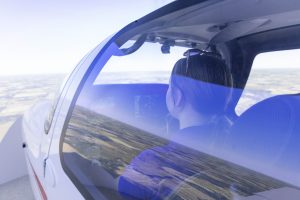 Student pilot seated in a training aircraft simulator during flight, with landscape visible through the window.