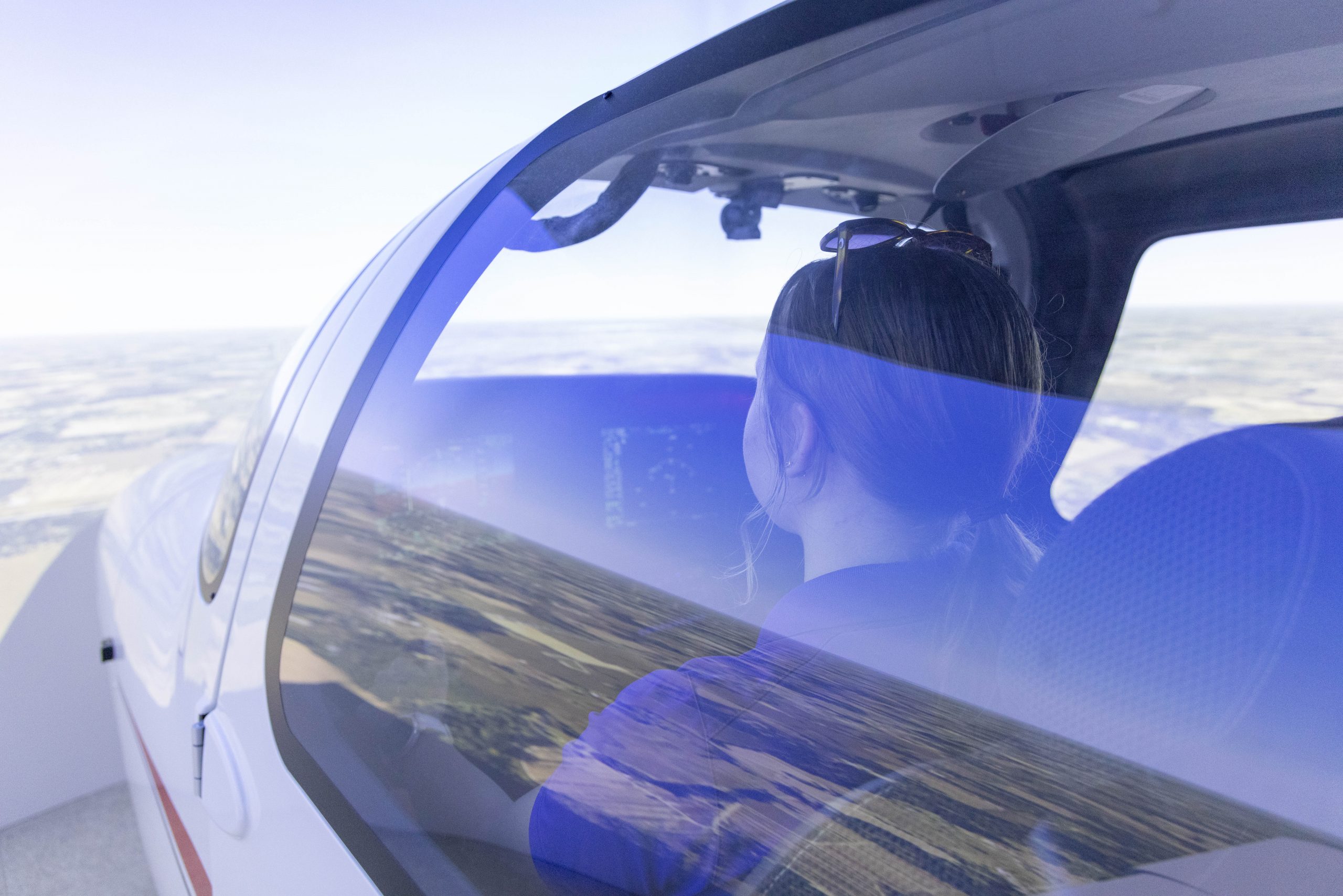 Student pilot seated in a training aircraft simulator during flight, with landscape visible through the window.