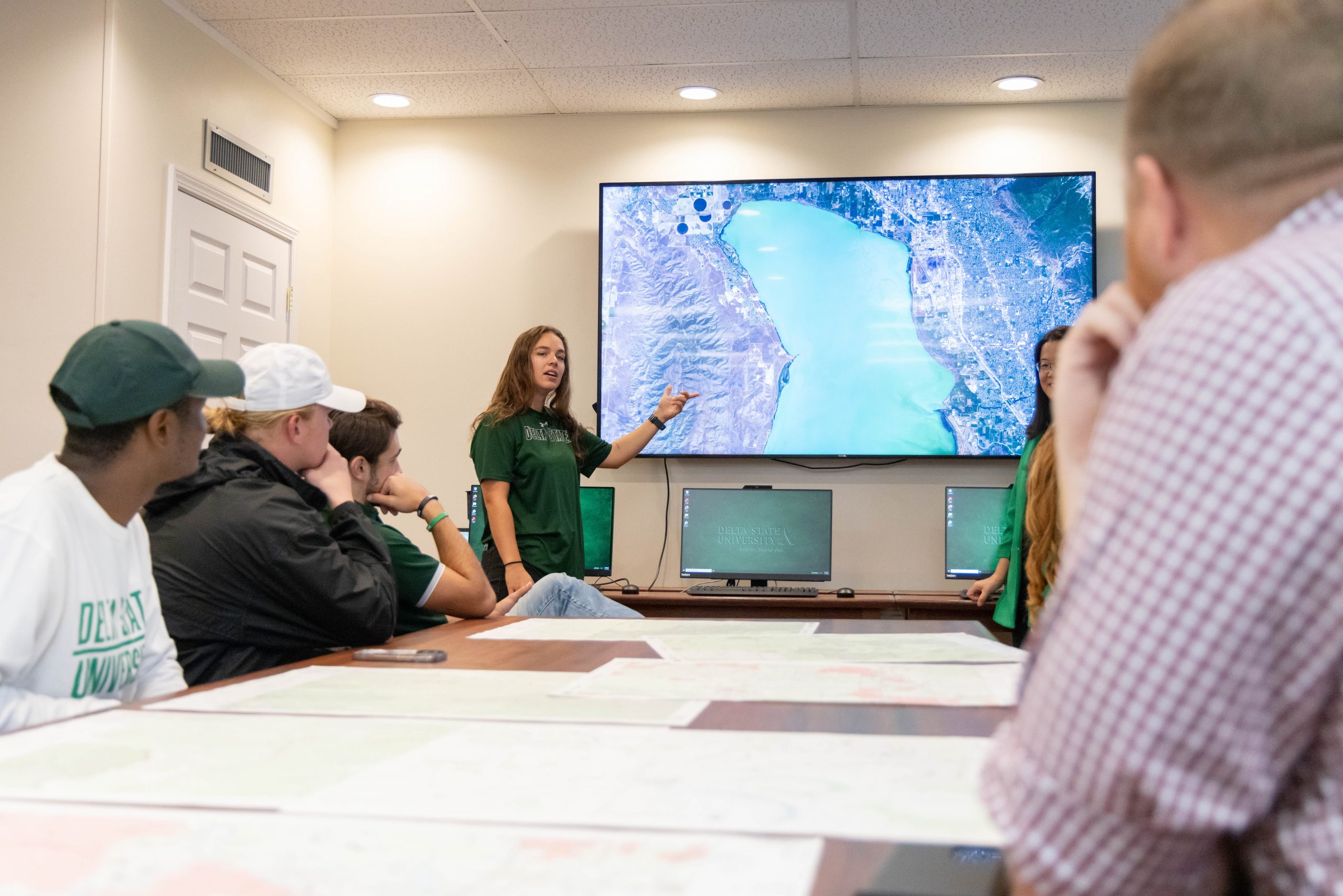 Student presenting a map on a large screen to classmates in a business lab.