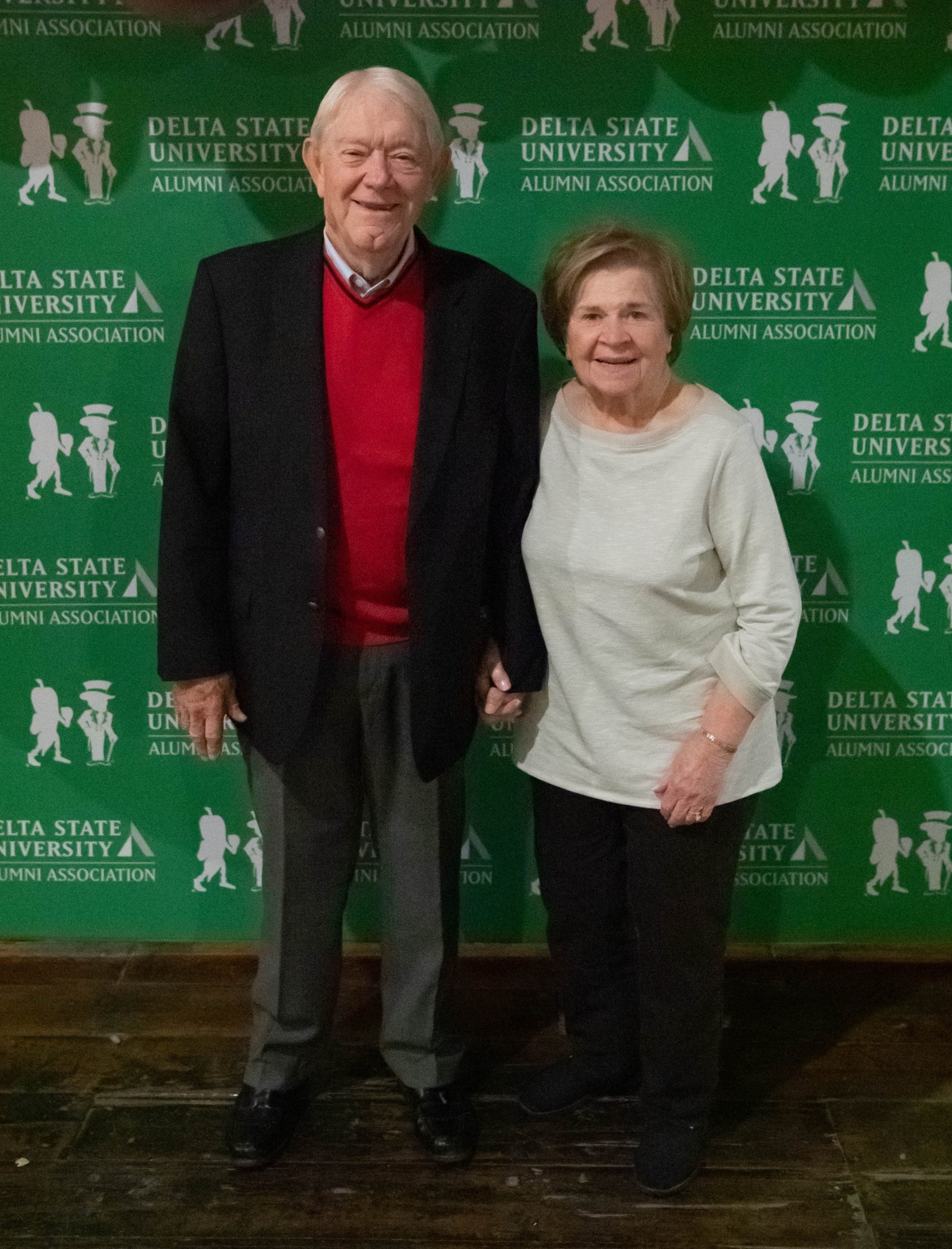 elderly couple standing in front of a green background.