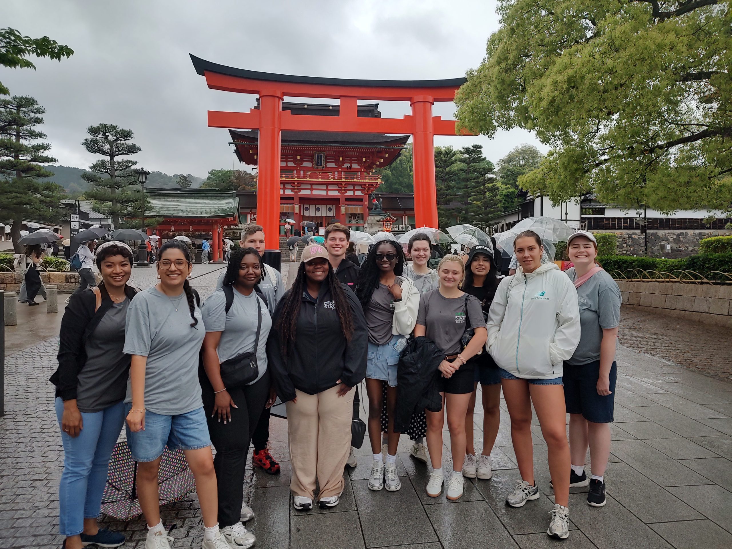 a group of students and faculty standing in front of a red arch in Japan.