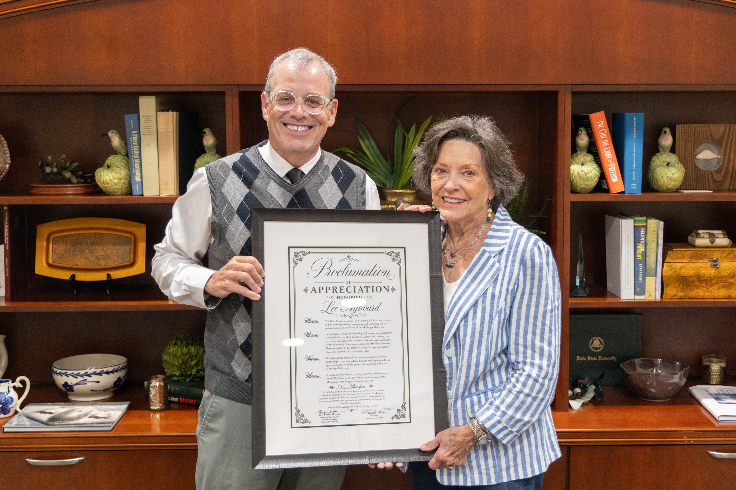 a college president presenting a large framed certificate to a female employee