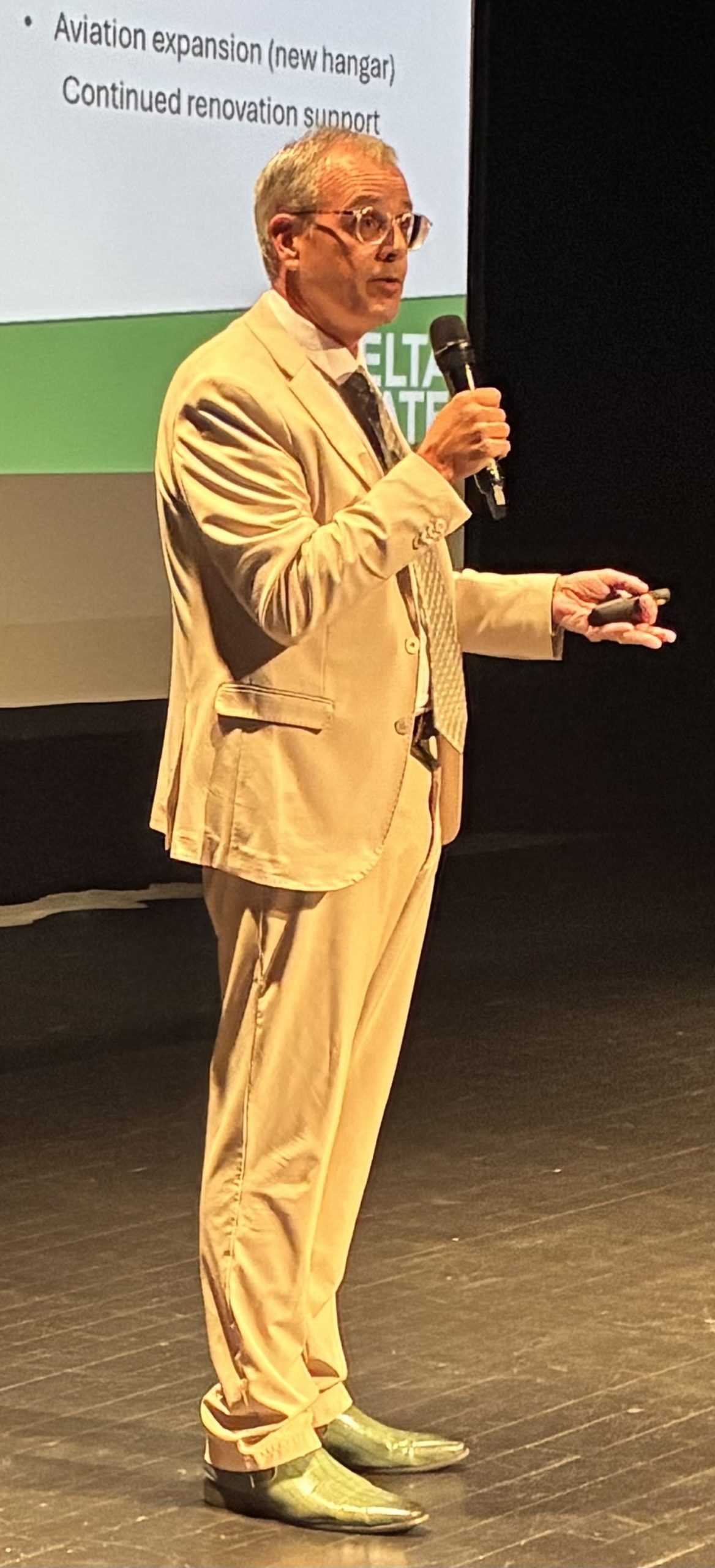 a college professor in a tan suit speaking into a microphone