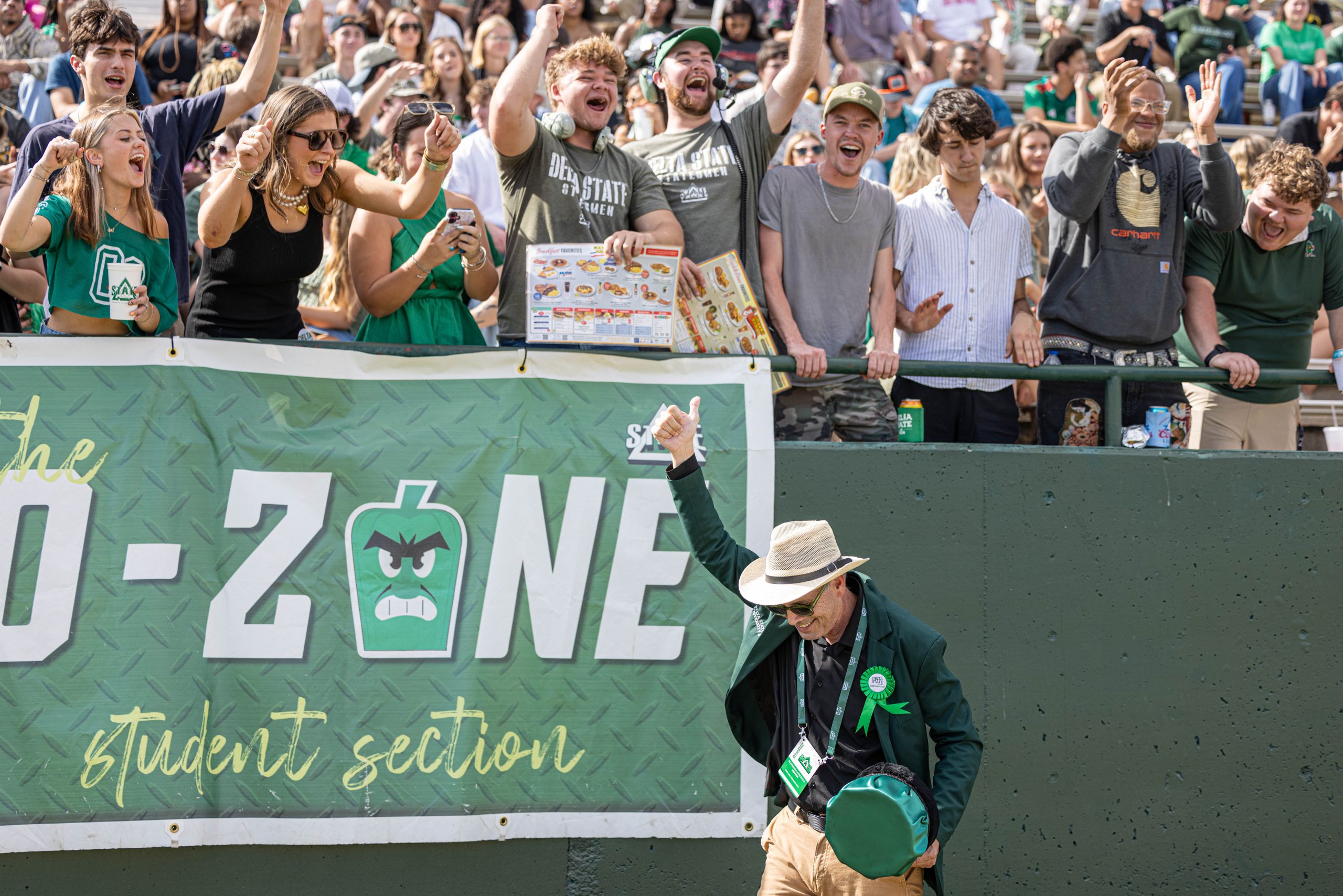 a university president in a green jacket rallying the student section at a football game.