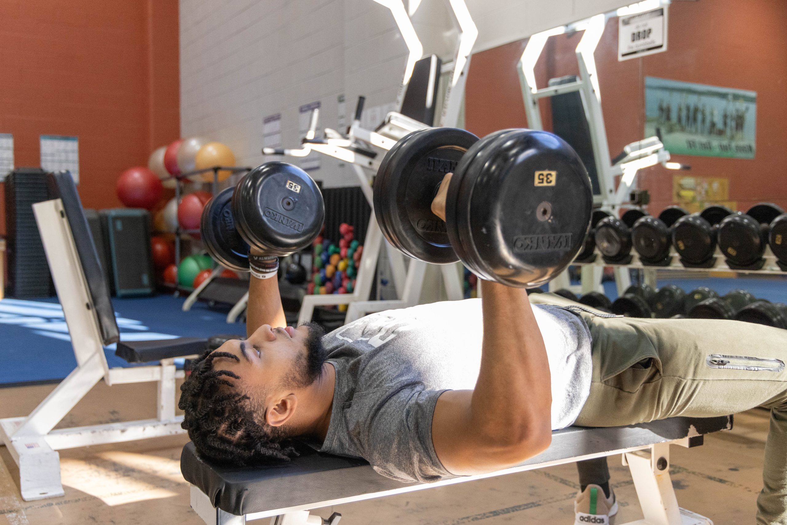 Student performing a dumbbell bench press in the fitness center.