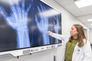 Graduate nursing student explaining X-ray images of a hand and wrist on a digital display.