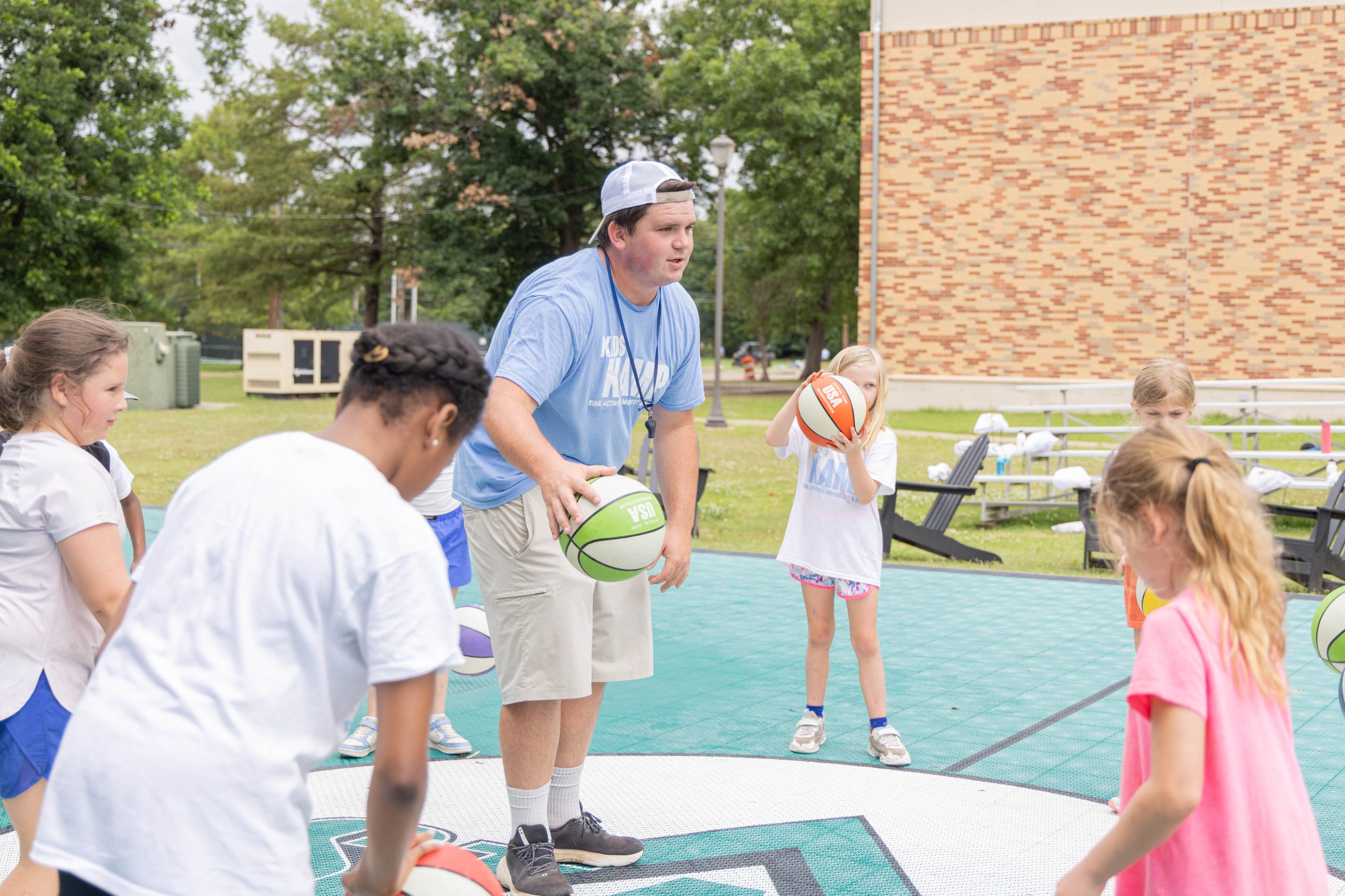 Delta State student leading children in a basketball activity on an outdoor court.