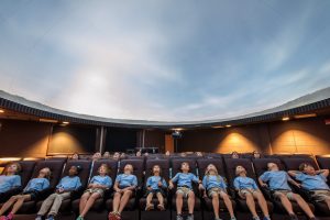 Students viewing a presentation projected onto the dome inside a planetarium.