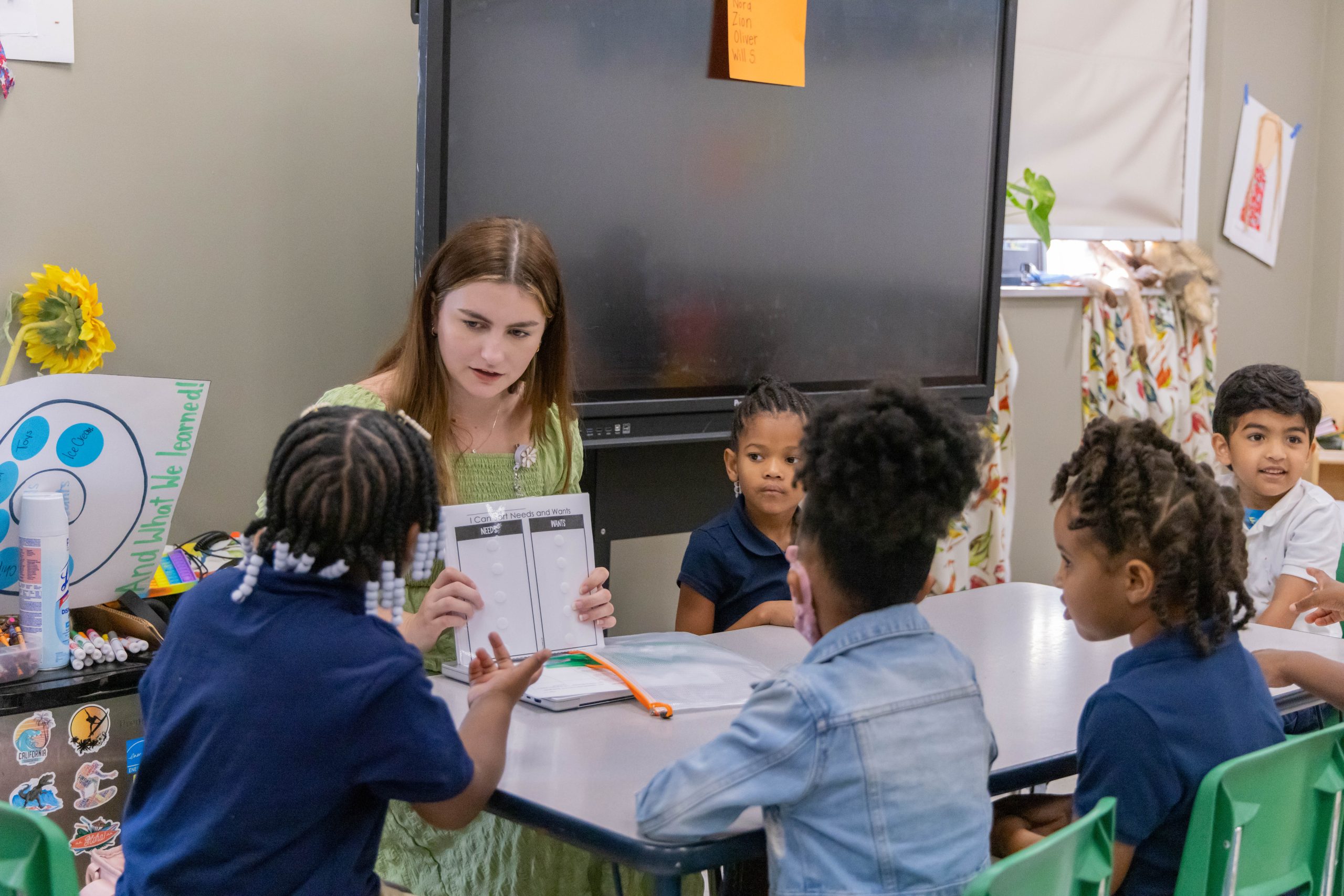 Teacher leading a small group activity with young students seated around a classroom table.