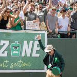 a university president in a green jacket rallying the student section at a football game.